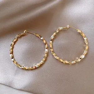 Detailed macro view of large golden hoop earrings featuring a faceted geometric texture.