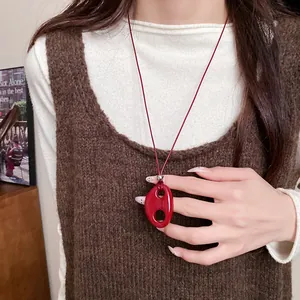Détail d'un collier pendentif ovale rouge en résine porté sur un gilet en maille brun