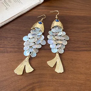 Dettaglio di orecchini a forma di pesce con scaglie di conchiglia e finiture dorate.