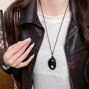 Détail du collier à pendentif ovale creux en résine noire sur une veste en cuir