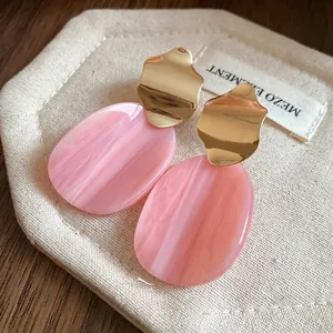 Irregular oval acrylic earrings with pink marble texture and gold wavy metal accent.