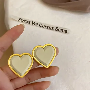 Primo piano dettagliato di orecchini a cuore con bordo dorato e finitura crema opaca