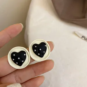 Primo piano di orecchini a lobo bianchi circolari con cuore nero e strass scintillanti.