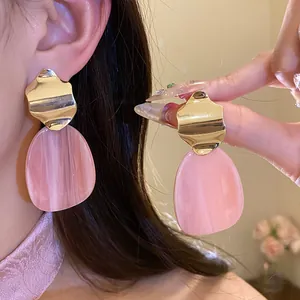 Close-up of irregular pink acrylic and gold metal earrings worn on ear