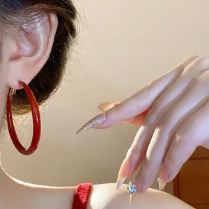 Close-up view of stylish retro Ankara red oil-dripped silver needle hoop earring on ear