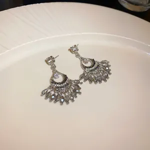 Dettaglio di orecchini d'argento con nappe di cristallo grigio su un piatto bianco