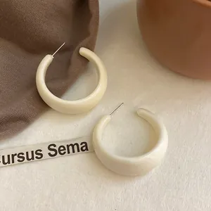 Eleganti orecchini a cerchio geometrici a C bianco crema con perni in argento su sfondo caldo.