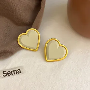Vista dettagliata di orecchini a lobo a cuore minimalisti con inserto beige e oro.
