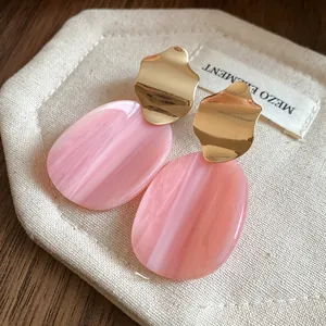 Detailed shot of irregular pink marbled acrylic and gold wavy metal earrings on fabric