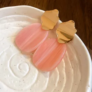 Detail view of pink marbled acrylic oval earrings with irregular gold metal tops