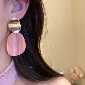 Close-up shot of pink acrylic petal drop earrings with irregular gold wave metal studs