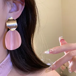 Detailed view of irregular oval pink acrylic earrings featuring gold wavy metal design.