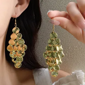 Detail view of gold sequin tassel earrings being worn and held by a model.