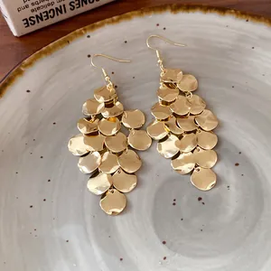 Detailed view of gold multi-layered hammered disc drop earrings on a ceramic plate.