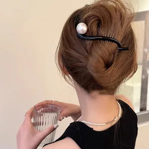 Détail d'une pince à cheveux noire en S avec une grande perle sur un chignon élégant