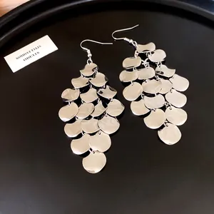 Macro view of silver tiered metal scale tassel drop earrings with mirror finish