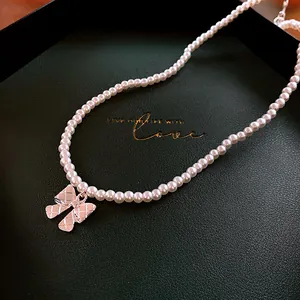 Close-up of an elegant pearl necklace featuring a silver quilted bow pendant on a green box