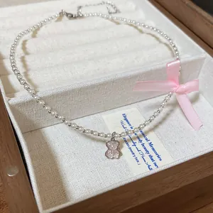 Detailed view of a pearl necklace with a pink bow and a cute bear-shaped pendant.