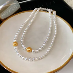 Detail view of a double-strand white pearl necklace with gold bead accents on a ceramic plate.