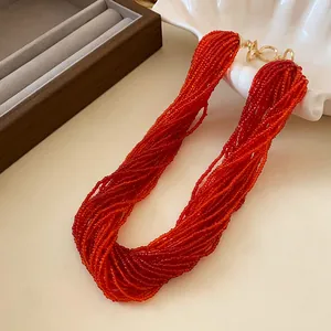 Macro detail showing the rich texture of a multi-layer red seed bead necklace with a gold clasp