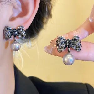 Close-up of vintage pleated bow earrings with grey pearl drop charms on ear and hand