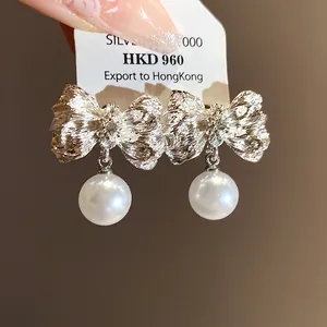 Detailed view of pleated silver bow earrings with elegant white pearl pendants
