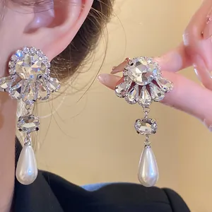 Primer plano de pendientes de flor plateados con cristales y perlas lágrima blancas.