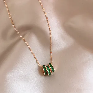 Close-up of a rose gold necklace featuring a pendant with three emerald-green gemstone rings.