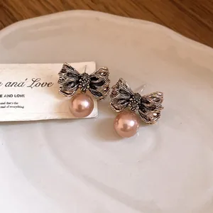 Detailed view of pleated bowknot earrings with pink pearl drop on ceramic plate