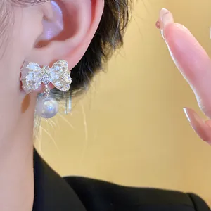 Close-up detail of textured silver bow earrings with a graceful white pearl pendant.