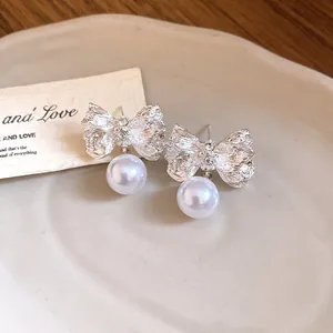 Detailed macro view of silver-toned wrinkled bow-knot earrings with elegant pearl pendants