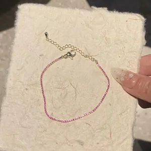 Close-up of ultra-thin pink zircon bracelet with gold chain on textured paper background.