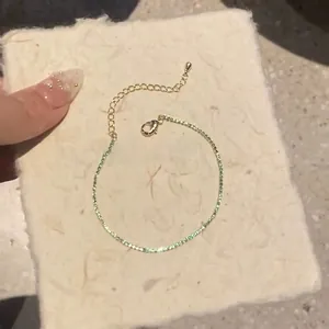 Detailed close-up of a dainty gold-plated bracelet with small green square zircons