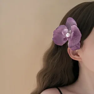 Detailed close-up view of a purple butterfly orchid hair clip with a pearl center on a model