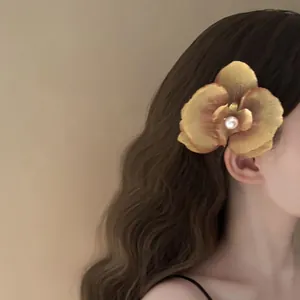 Detail view of a golden orchid flower hair clip with a pearl center on wavy hair