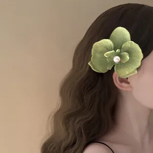 Close-up view of elegant green orchid flower hair clip with pearl on model's long wavy brown hair