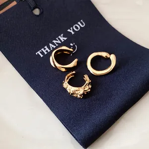 Close-up detail of three irregular textured gold ear cuffs on a navy blue thank you tag.