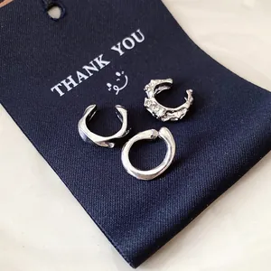 Close-up of three irregular silver ear cuffs set on a navy blue thank you gift card.