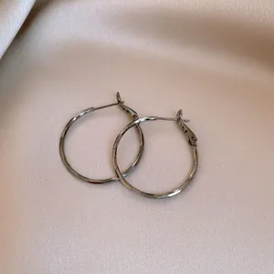 Detailed macro shot of minimalist textured gunmetal hoop earrings on cream satin background
