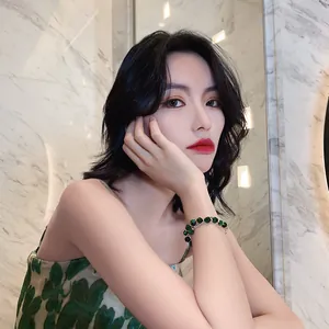 Elegantes Modell mit einem luxuriösen grünen Edelsteinarmband vor Marmorhintergrund