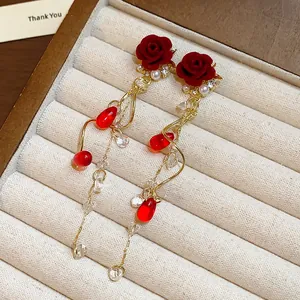 Primo piano di orecchini a rosa rossa con eleganti nappe dorate e piccole perle bianche