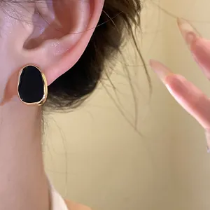 Close-up of elegant black enamel water drop stud earring with gold-toned rim on model's ear