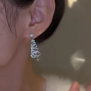 Close-up of a sparkling Christmas tree earring with red and green zircons on an ear.