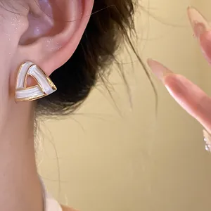 Detailed close-up showing a vintage white enamel triangle stud earring with elegant gold-tone trim