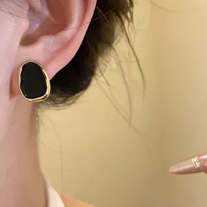 Close-up of French vintage black enamel stud earring with irregular gold rim on ear
