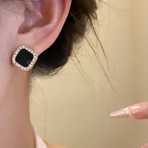 Close-up of a chic square black enamel stud earring with a sparkling rhinestone halo
