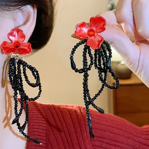 Detailed view of elegant red flower earrings featuring long black beaded tassels