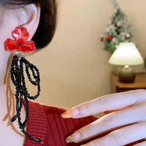 Close-up of red flower crystal stud earrings featuring long black beaded tassels on model.