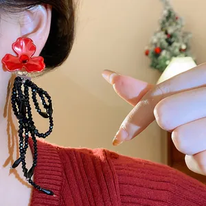 Close-up of red flower earrings with long black beaded tassels on a model's ear