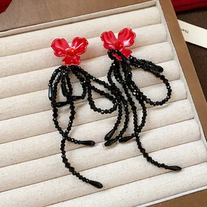 Close-up of red flower stud earrings with elegant black beaded long tassels on display